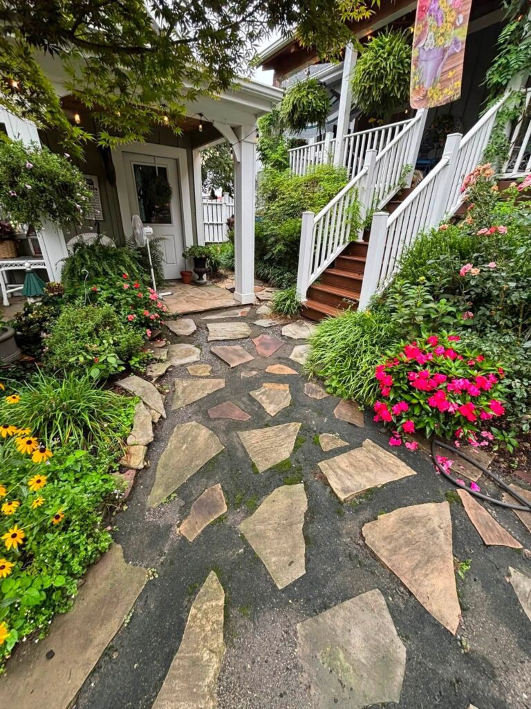Irregular flagstone walkway set in gravel leading to a white porch and stairs, bordered by impatiens and black-eyed Susans.